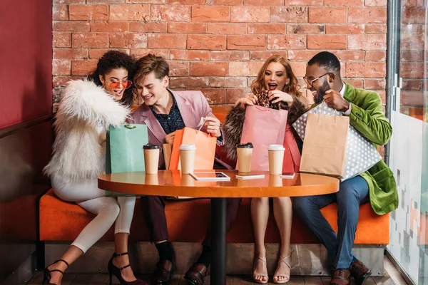 Sorrindo Moda Jovens Multiétnicos Olhando Sacos Papel Enquanto Bebem Café — Fotografia de Stock