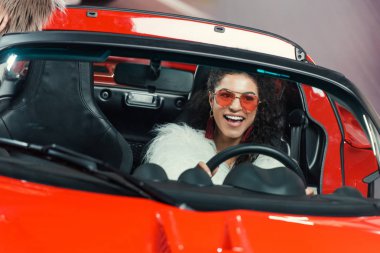 happy stylish young african american woman in fur coat driving luxury luxury car clipart