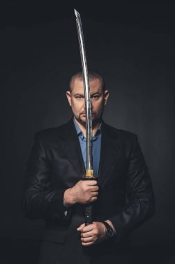 Japon katana kılıcı yüzünü siyaha izole önünde tutan takım elbiseli olgun adam