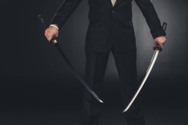 koyu arka plan üzerinde çift katana kılıçlı takım elbiseli adam kırpılmış atış