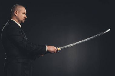 side view of man in suit with katana sword isolated on black clipart