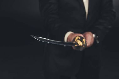 cropped shot of man in suit with katana sword on dark background clipart