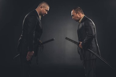 side view of modern samurai in suits bowing to each other isolated on black clipart