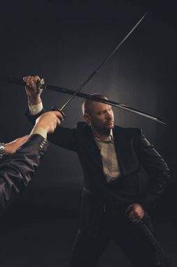 strong mature businessman fighting with katana sword isolated on black clipart