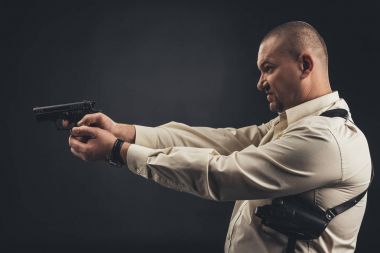 side view of man in shirt holding gun isolated on black clipart