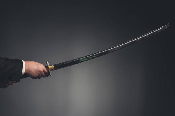 cropped shot of man holding katana sword on black