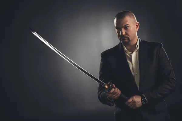 mature man in suit with katana sword on black
