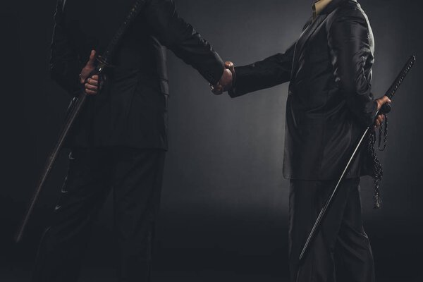 обрезанный снимок членов якудза пожимающих руки с катанами за спиной изолированных на черном
