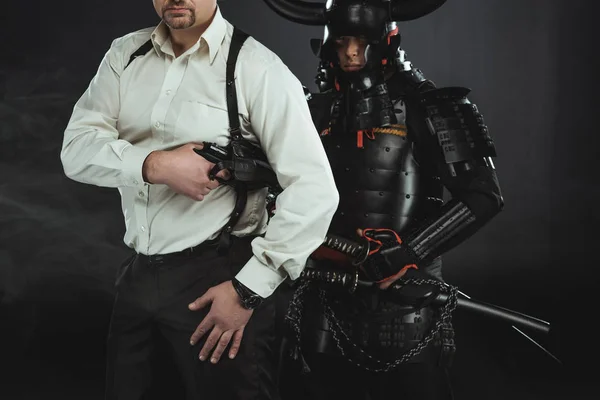 cropped shot of man with gun and samurai behind him on black