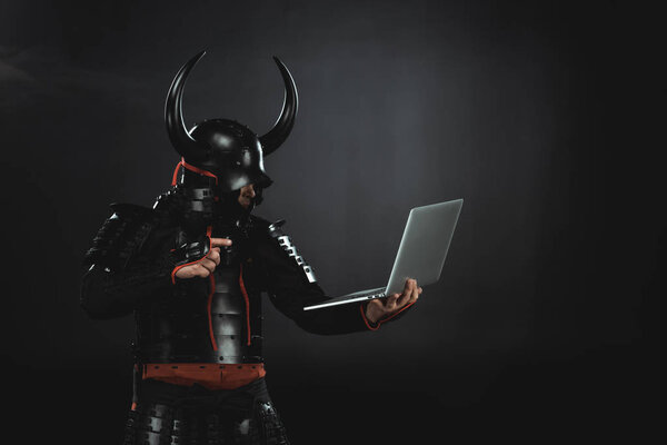 side view of armored samurai using laptop on black