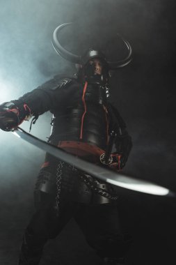 bottom view of samurai in traditional armor with sword on dark background with smoke clipart