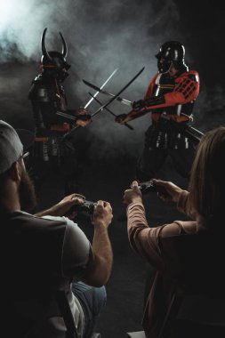 back view of man and woman playing samurai fighting in real life with gamepads on black clipart