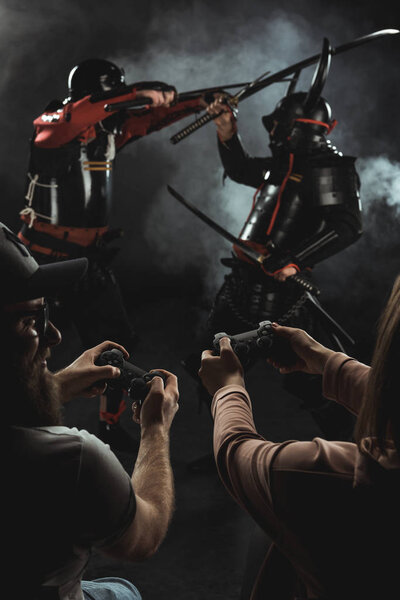 back view of man and woman playing samurai fighting in real life with gamepads on black