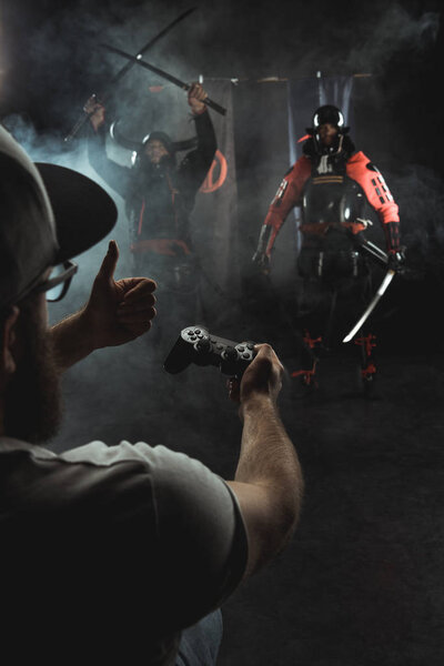 mature man playing samurai fighting with gamepad in real life and showing thumb up to characters