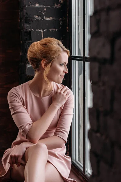 窓辺に座っているピンクのドレスで思いやりのある若い女性 — ストック写真