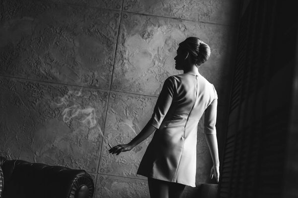 black and white shot of attractive young woman in dress in front of concrete wall