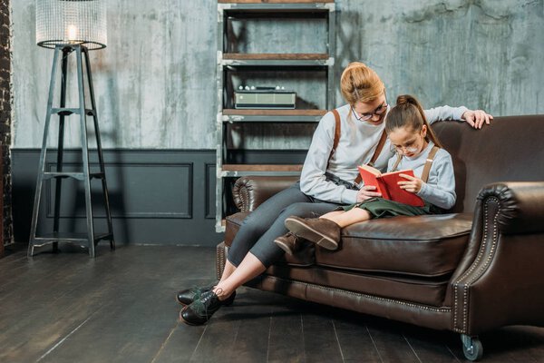 mother and daughter reading book together on couch