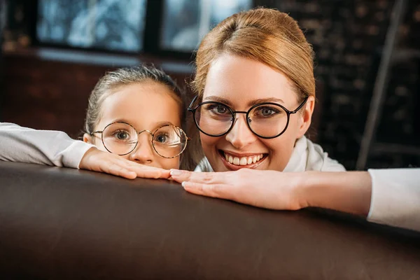 Mãe Filha Óculos Olhando Para Câmera Enquanto Esconde Atrás Sofá — Fotografia de Stock