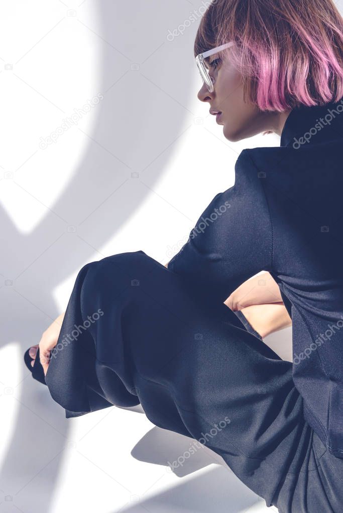 side view of fashionable girl with pink hair sitting on white