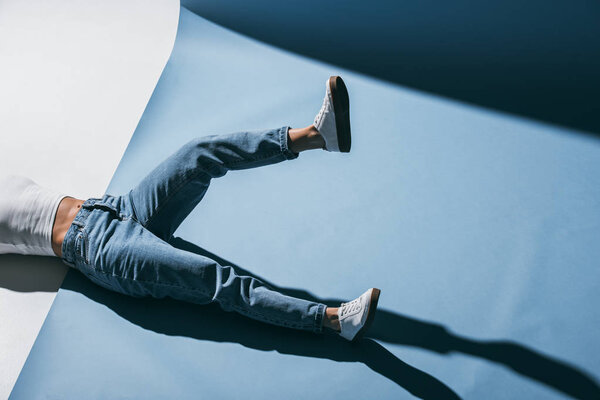 cropped image of stylish girl lying on floor in jeans with one leg raised