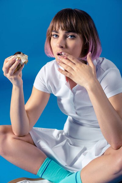 привлекательная спортсменка ест кусок пирога изолированный на голубом
