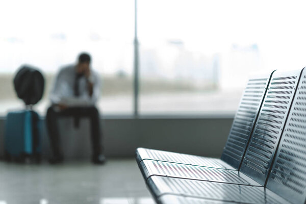 close-up shot of seats at airport lobby with buisnessman waiting for plane blurred on background