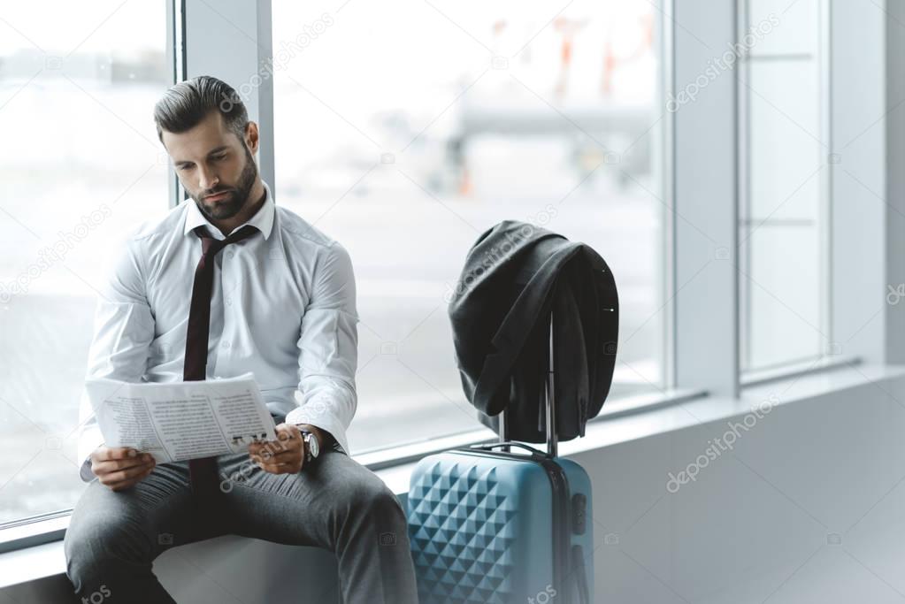 young businessman reading newspaper while waiting for flight at airport lobby