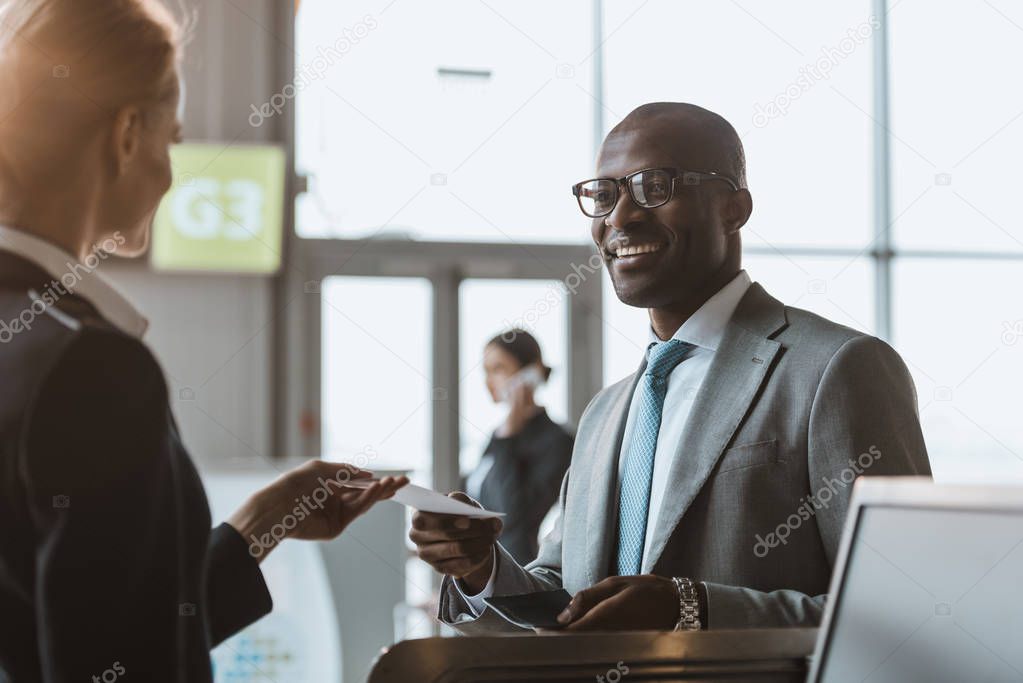 happy young businessman giving passport and ticket to staff at airport check in counter