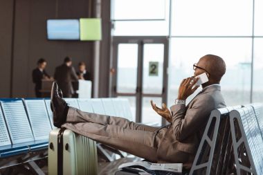businessman talking by phone while waiting for flight at airport lobby clipart