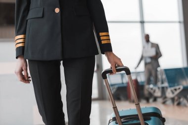 cropped shot of female pilot with suitcase walking by airport lobby clipart
