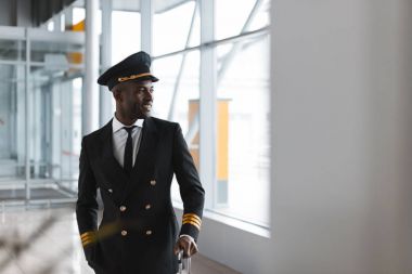 handsome young pilot with luggage at airport looking away clipart