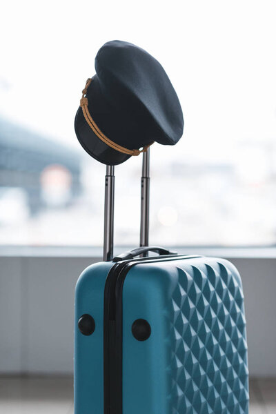 pilot cap hanging on handle of suitcase at airport