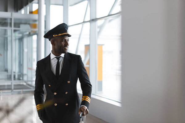 handsome young pilot with luggage at airport looking away
