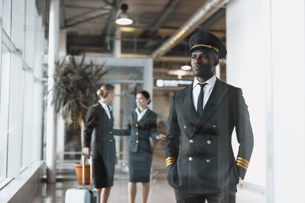 thoughtful young pilot in airport with stewardesses before flight