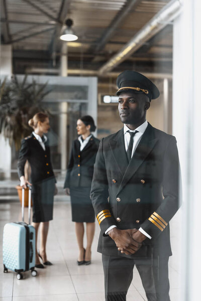 handsome young pilot in airport with stewardesses before flight