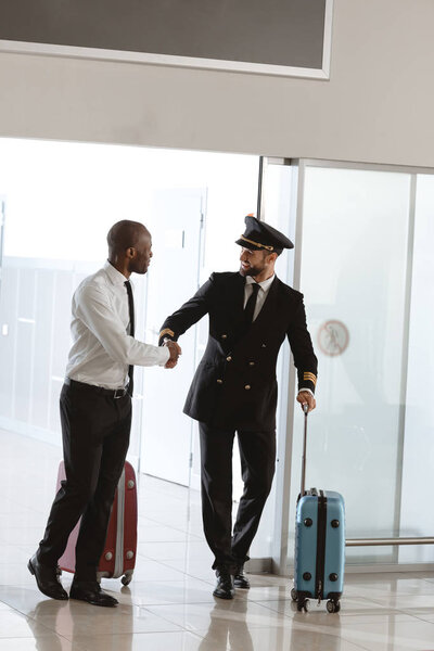 handsome pilot handshaking with young businessman at departure area of airport