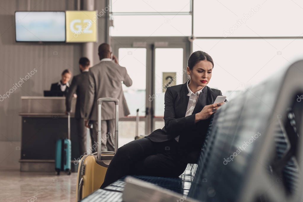 young businesswoman waiting for plane at airport lobby and using smartphone