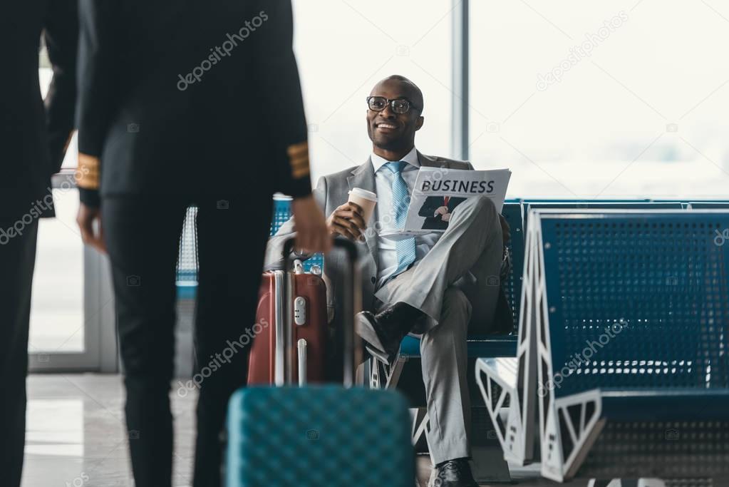 handsome young businessman looking at female pilot passing by while wait for flight at airport lobby