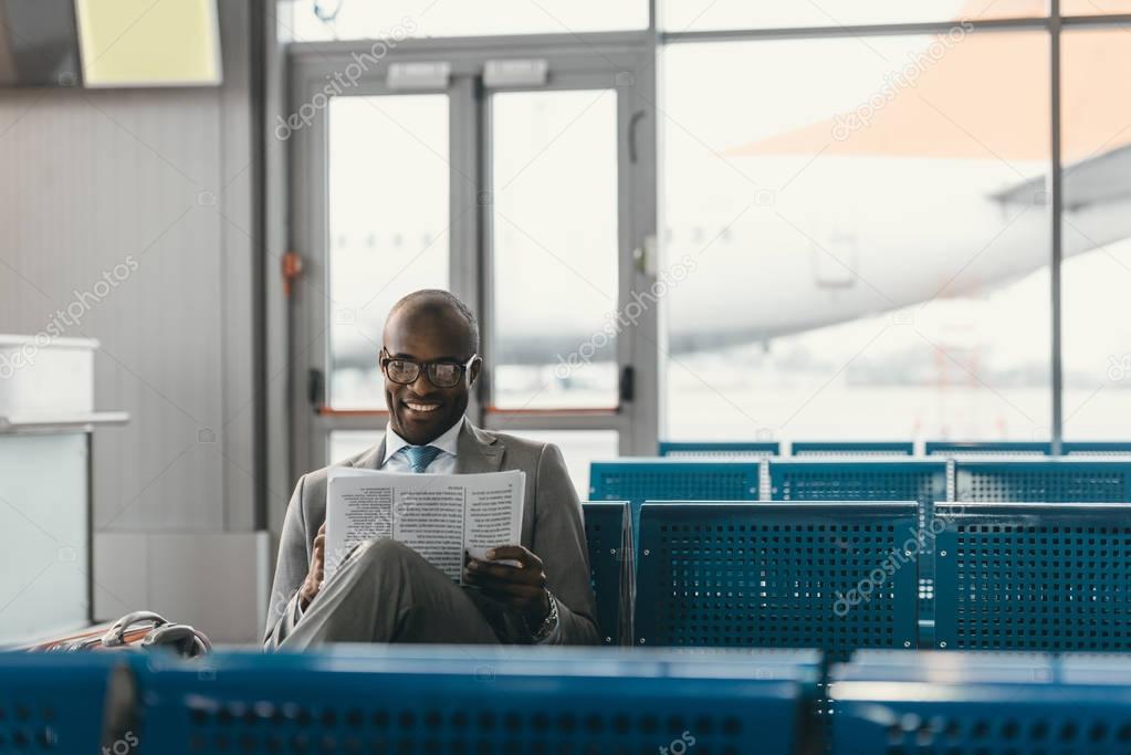 handsome businessman reading newspaper while waiting for flight at airport lobby