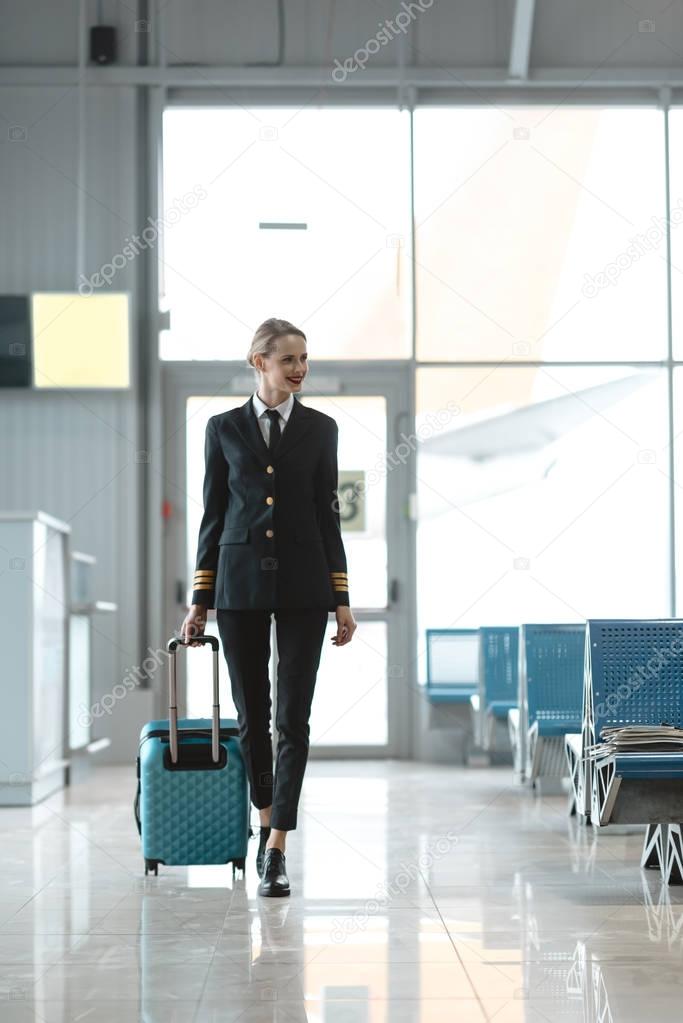 beautiful female pilot with suitcase walking by airport lobby