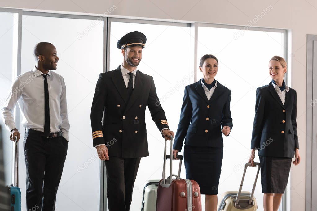 happy aviation personnel team walking by airport loggy with suitcases