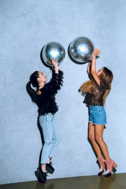 side view of fashionable young women having fun with shiny silver balloons clipart