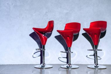 three red empty bar stools near grey wall clipart