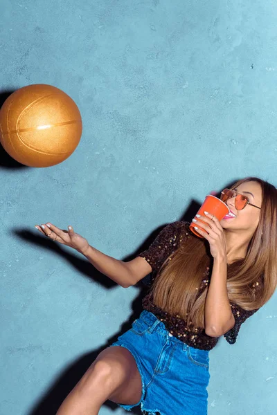 Mujer Afroamericana Con Taza Desechable Lanzando Pelota Baloncesto Oro — Foto de stock gratis