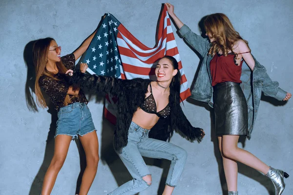 コンクリートの壁にアメリカ国旗を持つ多文化の若い女性  — 無料ストックフォト