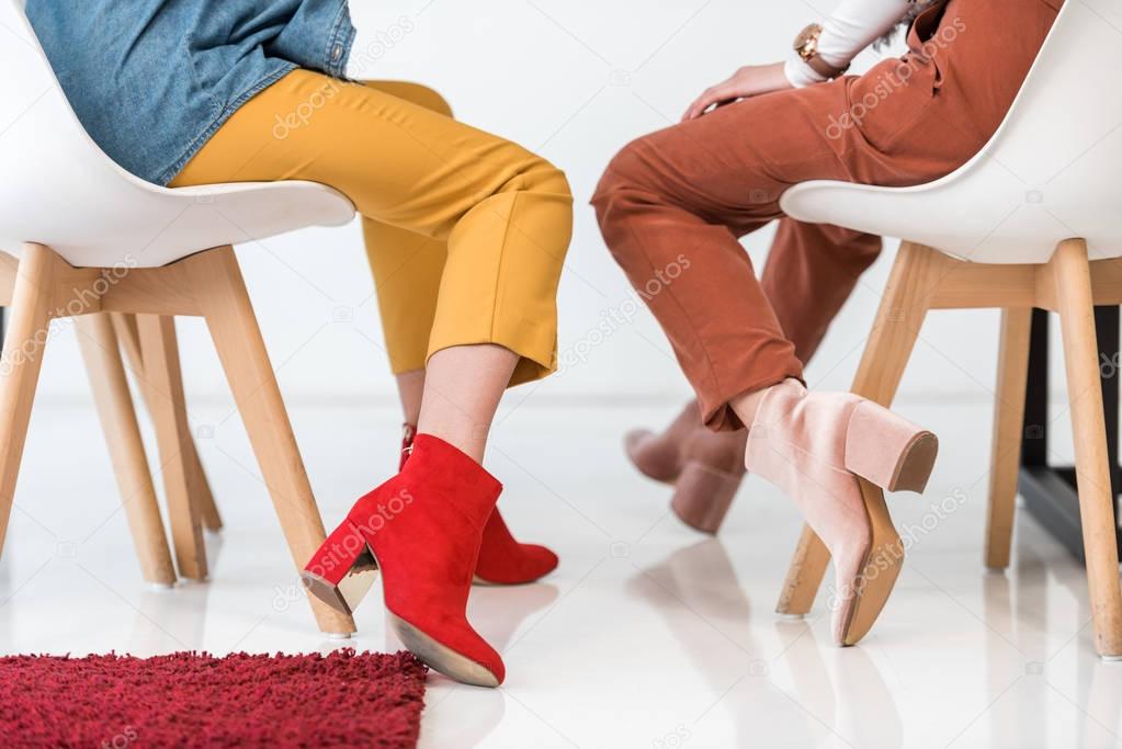 cropped view of stylish women in trendy shoes sitting on chairs