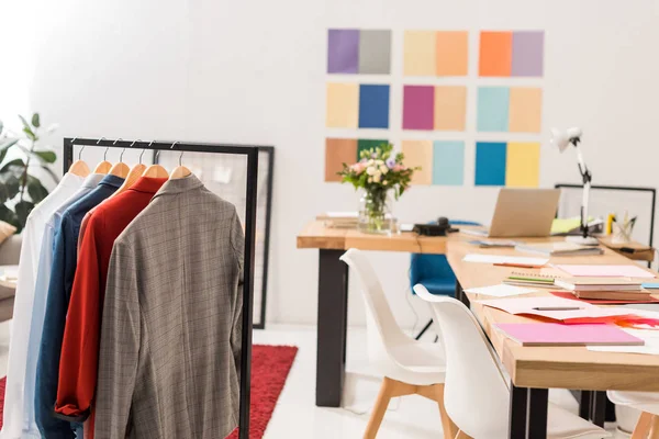 fashionable clothes on hangers,  paperwork on table in modern office with color palette on wall