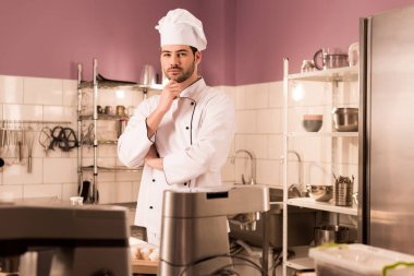 portrait of pensive confectioner standing at counter in restaurant kitchen clipart