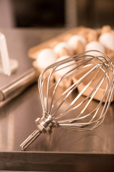 close up view of whisk and raw eggs for making cream on counter in restaurant