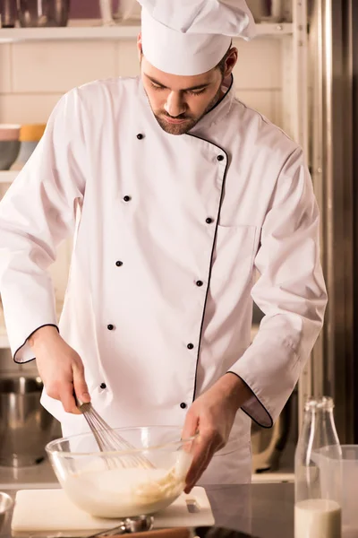 focused confectioner in chef hat making dough in restaurant kitchen